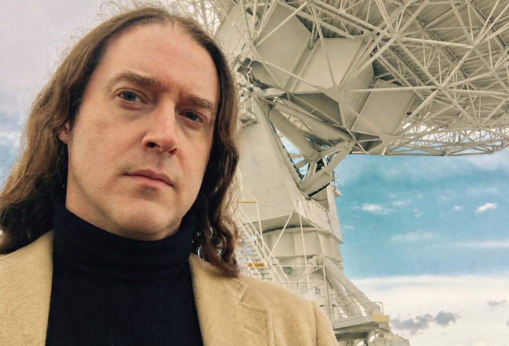 Daniel McShan, PhD, in professional attire with a large satellite dish in the background